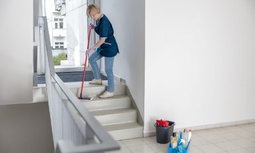 Cleaning lady in uniform with mop and rag washes a dusty steps of the house . High quality photo